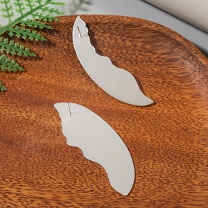 Detail view of matte silver asymmetric wave earrings with sandblasted texture on wood