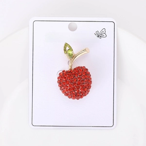 Macro detail of a red rhinestone apple brooch on a white fashion jewelry display card