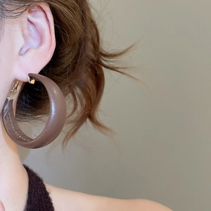 Detail of brown leather C-shaped hoop earrings featuring fine stitching and gold hardware