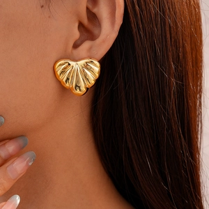 Close-up of a golden seashell-shaped earring with elegant textured details on a model