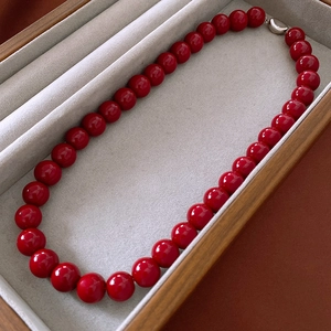 Close-up of red round beaded necklace with silver clasp in a grey velvet jewelry box