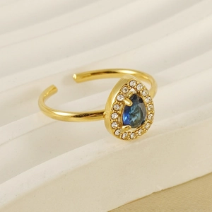 Détail d'une bague en acier doré avec zircon bleu en forme de goutte et halo de pierres