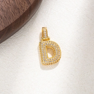 Macro detail of gold letter D pendant with micro-paved zircons on textured background