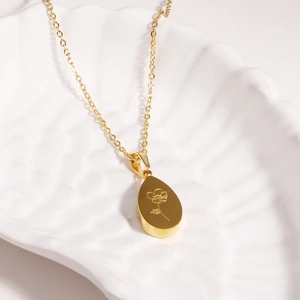 Collier français en acier titane doré avec pendentif fleur goutte sur fond de coquillage