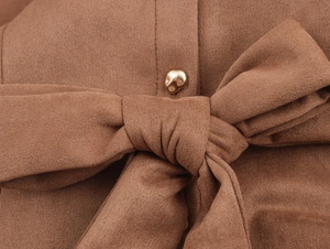 Detail of brown faux suede fabric featuring a large bow tie and a gold metal button
