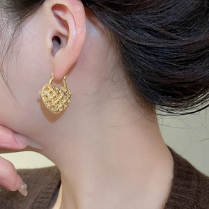 Close-up of golden hollow heart earrings with grid texture on a female model