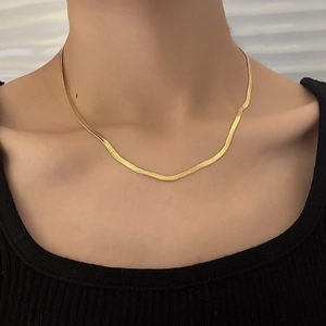 Close-up of golden flat snake bone layered necklace on a model wearing black knitwear