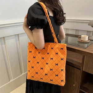Orange corduroy tote bag with black bow pattern carried by a model in a home setting