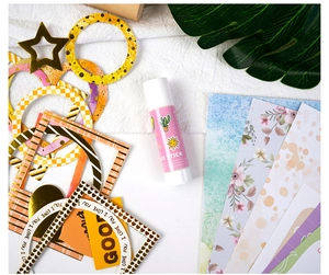 Detail showing white glue stick and various decorative paper cutouts for DIY scrapbooking