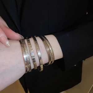 Detailed view of five gold-toned stackable bangles with geometric patterns and LOVE engraving