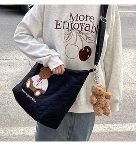 Detail of black quilted tote bag with teddy bear embroidery and brown plush keychain