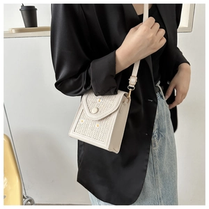 White woven shoulder bag with daisy patterns worn by model in a stylish indoor setting