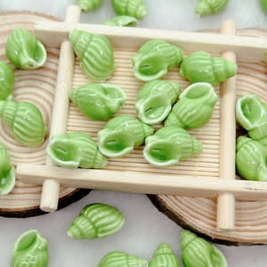 Macro shot of green shell-shaped ceramic beads for DIY jewelry making on a bamboo tray