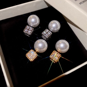 Macro detail of luxury pearl and square zircon earrings on a black velvet display background