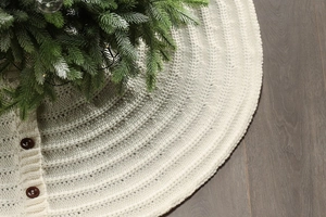 Detail of cream white cable knit Christmas tree skirt with wooden buttons on wood floor