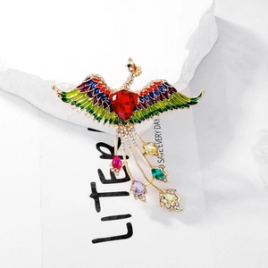Detailed close-up of a vintage gold phoenix brooch with colorful enamel and heart-shaped stone
