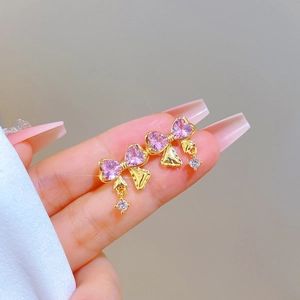 Dettaglio di orecchini a fiocco dorati con pietre a cuore rosa e diamanti rotondi