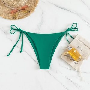 Detail view of dark green tie-side bikini bottom on marble with summer vacation props