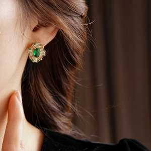 Gros plan de boucles d'oreilles losanges dorées avec pierre verte et zircon sur l'oreille