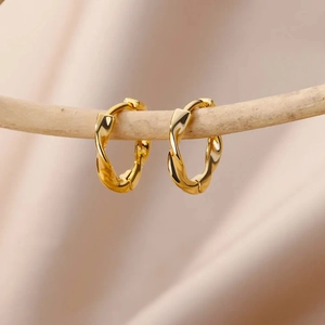 Polished 18K gold wave twisted hoop earrings for women hanging on a wooden branch