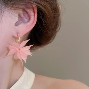 Detailed view of pink acrylic flower petal earrings with golden metal hoop worn by a model