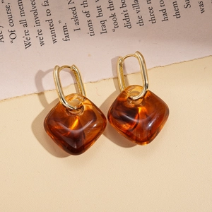 Close-up of vintage amber resin square drop earrings with gold hoops on retro newspaper