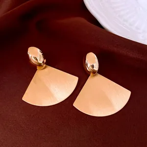 Golden oval fan-shaped brushed earrings on white ceramic dish with silk background