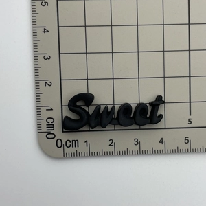 Detailed size measurement of black Sweet resin letter charm on a metric ruler scale