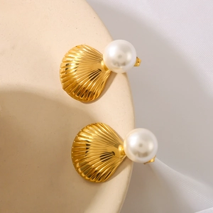 Elegant gold shell earrings with large white pearls on a minimalist ceramic dish