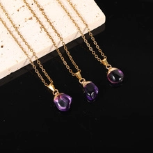 Three gold necklaces with purple crystal mushroom pendants on a beige stone surface
