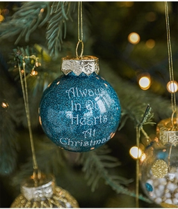 Close-up of a blue glitter Christmas ball with white lettering on a green tree branch