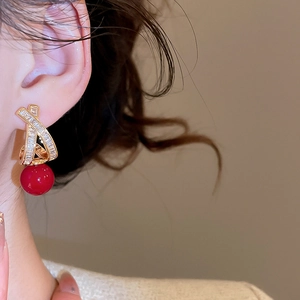 Detail of cross-shaped gold earrings with zircons and a large red bead on a model