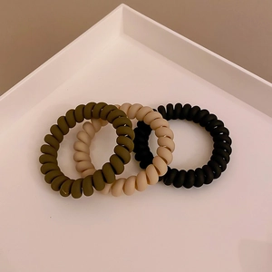 Three matte spiral hair ties in olive green, beige, and black on a white tray