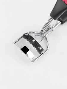 Detail view of silver stainless steel eyelash curler with built-in black comb on white background