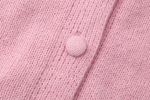 Macro detail of a pink knitted cardigan showing texture and a fabric-covered button