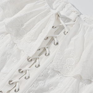 Dettaglio del top in cotone bianco con ricamo floreale e allacciatura sul retro