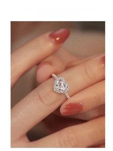Close-up of heart-shaped moissanite ring with halo setting on finger