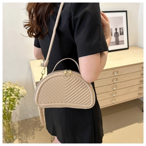 Detailed view of beige half-moon bag featuring V-shaped quilting and gold metal zippers