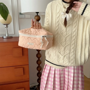 Dettaglio del beauty case beige trapuntato a cuori con manico superiore e etichetta Suzakku