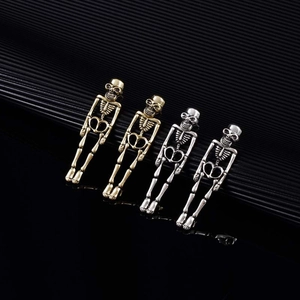 Macro shot showing golden and silver metal skeleton skull earrings on black background