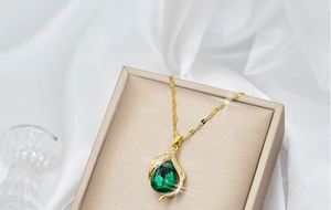 Close-up of golden teardrop necklace with emerald green stone in a jewelry box