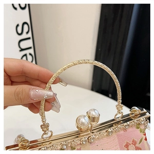 Detailed macro view of the gold carved handle and pearl clasp on a pink floral clutch bag