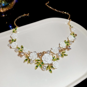 Macro detail of floral necklace with white roses, pearls and crystals on a white ceramic tray
