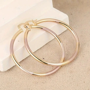 Macro-opname van grote driekleurige metalen oorringen in goud, roségoud en zilver-look