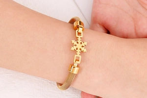 Détail d'un bracelet en maille dorée avec pendentif flocon porté au poignet d'un mannequin