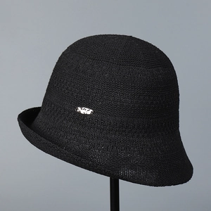Close-up of black knitted bucket hat with hollow texture and small metal oval emblem