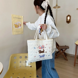 Detailed close-up of cute cat and bow embroidery on creamy white quilted handbag fabric