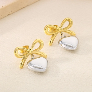Detail of gold bow earrings with silver heart pendants on beige silk fabric