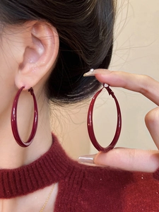 Close-up of model wearing dark red large hoop earrings with smooth lacquer finish