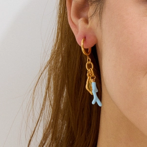 Detail of gold hoop earrings with blue coral pendants on model from a side profile